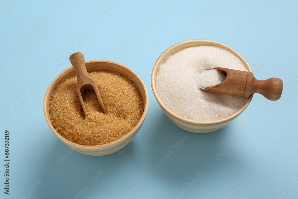 Bowls with different types of sugar on blue background