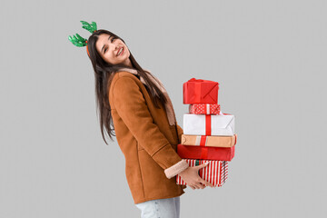 Poster - Young woman in reindeer horns with Christmas presents on light background