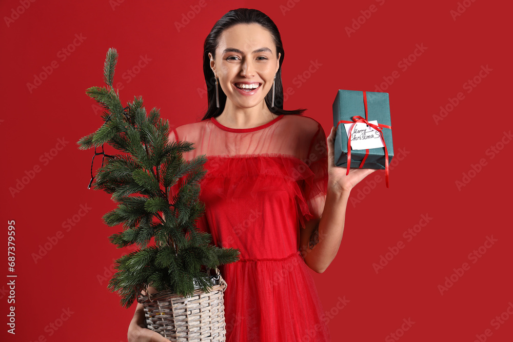 Beautiful woman with Christmas tree and present on red background