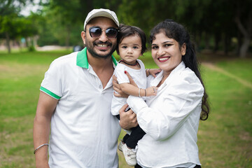 Wall Mural - Happy Young indian parents with their cute little adorable daughter enjoying in park or garden. lifestyle concept.