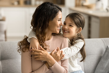 Wall Mural - Happy pretty loving little kid girl hugging positive mom, playing with parent at home. Beautiful mother piggybacking sweet child, playing active family game, laughing