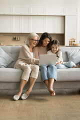 Canvas Print - Positive excited grandmother, mom and little tween child using laptop on home couch together, watching online content, movie, enjoying Internet service, communication, digital entertainment