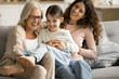 © fizkes - Happy joyful grandma and mom playing with cheerful kid girl on sofa, tickling laughing child, having fun, enjoying home family activity, closeness, bonding, playtime