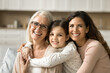 © fizkes - Cheerful attractive grandmother, mother and granddaughter kid hugging with love, enjoying bonding, close relationship, family leisure, looking at camera with perfect toothy smiles