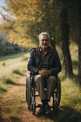 Poster - A handsome Italian, happy smiling disabled man of 60-70 years old is sitting in a wheelchair in nature against a background of trees in sunny weather.