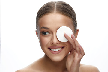 Wall Mural - Close up beauty portrait of a young attractive woman cleaning her face with a cotton pad isolated over white background