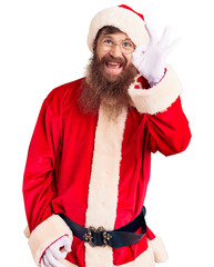 Poster - Handsome young red head man with long beard wearing santa claus costume smiling positive doing ok sign with hand and fingers. successful expression.