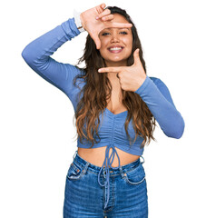 Wall Mural - Young hispanic girl wearing casual clothes smiling making frame with hands and fingers with happy face. creativity and photography concept.