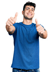 Poster - Young hispanic man wearing casual t shirt approving doing positive gesture with hand, thumbs up smiling and happy for success. winner gesture.