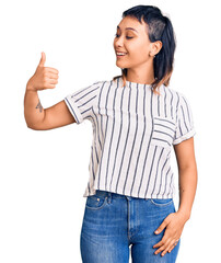 Canvas Print - Young woman wearing casual clothes looking proud, smiling doing thumbs up gesture to the side