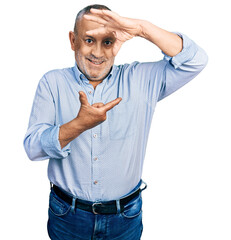 Canvas Print - Senior man with grey hair and beard wearing casual blue shirt smiling making frame with hands and fingers with happy face. creativity and photography concept.