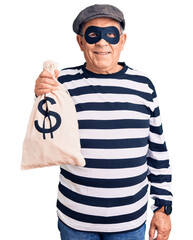 Wall Mural - Senior handsome man wearing burglar mask holding money bag looking positive and happy standing and smiling with a confident smile showing teeth