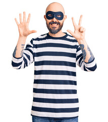 Sticker - Young handsome man wearing burglar mask showing and pointing up with fingers number eight while smiling confident and happy.