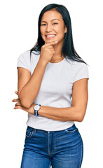 Wall Mural - Beautiful hispanic woman wearing casual white tshirt looking confident at the camera smiling with crossed arms and hand raised on chin. thinking positive.