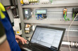 © Alexandr - Programmer of PLC checks correct function of program in PLC with electrical cabinet in background
