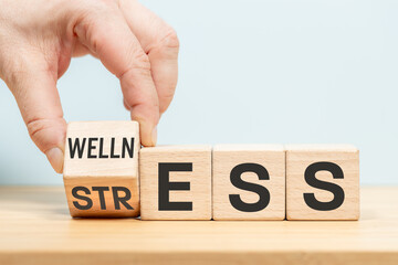 Stress or Wellness word concept on wooden cubes. Symbol of stress or well-being. Businessman hand turns the dice. blue background, copy space, business stress or well-being concept