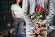 Asian man hiding roses to surprise his girlfriend on dating in Valentine's, Anniversary or birthday, focus on flower, attractive couple having romantic on rooftop