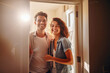 Portrait of cheerful couple inviting guests to enter home, happy young guy and lady standing in doorway of modern flat.
