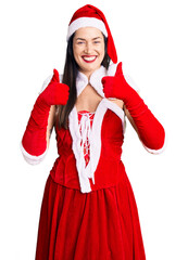 Wall Mural - Young beautiful caucasian woman wearing santa claus costume success sign doing positive gesture with hand, thumbs up smiling and happy. cheerful expression and winner gesture.