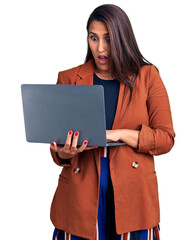 Canvas Print - Young beautiful brunette woman using laptop scared and amazed with open mouth for surprise, disbelief face