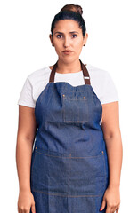 Sticker - Young beautiful brunette woman wearing apron with serious expression on face. simple and natural looking at the camera.