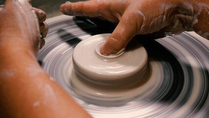 A potter's stained hands shape a stunning pot from white clay on the wheel. Working in a pottery workshop. The concept of handicraft, art and craft.