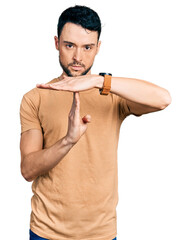 Canvas Print - Hispanic man with beard wearing casual t shirt doing time out gesture with hands, frustrated and serious face