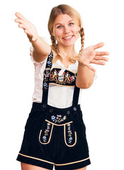 Wall Mural - Young beautiful blonde woman wearing oktoberfest dress looking at the camera smiling with open arms for hug. cheerful expression embracing happiness.