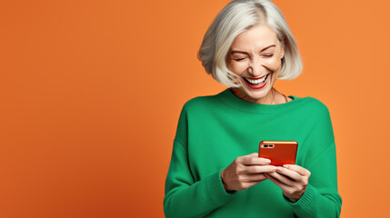 Canvas Print - An elderly woman smiling and laughing with her phone against orange background.