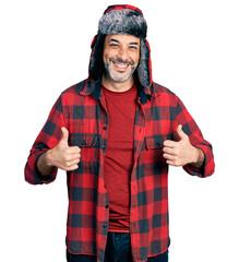 Canvas Print - Middle age hispanic man with grey hair wearing fluffy earmuff hat success sign doing positive gesture with hand, thumbs up smiling and happy. cheerful expression and winner gesture.