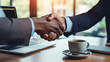 Two individuals are shaking hands over an office desk , signifying a professional agreement or partnership.
