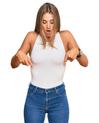 Wall Mural - Young blonde woman wearing casual style with sleeveless shirt pointing down with fingers showing advertisement, surprised face and open mouth