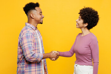 Poster - Young couple two friends family man woman of African American ethnicity wear casual clothes together hold hands folded handshake gesture isolated on plain yellow background. Friendship greet concept.