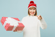 Merry elderly woman 50s year old iin sweater red hat posing hold present box with gift ribbon bow point finger camera on you isolated on plain blue background Happy New Year Christmas holiday concept