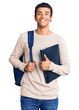 © Krakenimages.com - Young african amercian man wearing student backpack holding binder looking positive and happy standing and smiling with a confident smile showing teeth