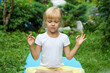 blonde little girl in a white T-shirt does yoga on a blue mat in the garden. a child and a healthy lifestyle