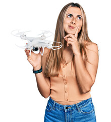 Sticker - Hispanic young woman holding drone serious face thinking about question with hand on chin, thoughtful about confusing idea