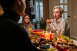 Elegant middle-aged mother-in-law celebrating Christmas with family, chatting at dinner holiday table in dark living room with cozy interior on xmas eve. Concept of home festive atmosphere.