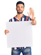© Krakenimages.com - Young handsome hispanic man holding cardboard banner with blank space with open hand doing stop sign with serious and confident expression, defense gesture