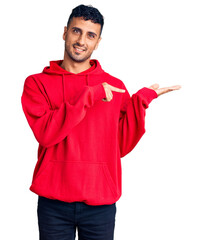 Sticker - Young hispanic man wearing casual clothes amazed and smiling to the camera while presenting with hand and pointing with finger.