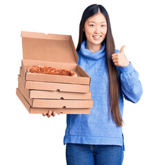 Poster - Young beautiful chinese woman holding cardboard boxes of italian pizza smiling happy and positive, thumb up doing excellent and approval sign