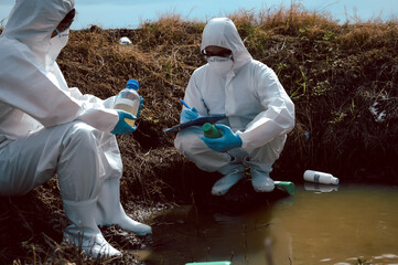 Team of scientists or biologists wears protective clothing to collect water samples from a natural water source with chemical-filled bottles of trash. Water pollution concept.