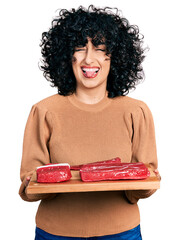 Canvas Print - Young middle east girl holding board with raw meat winking looking at the camera with sexy expression, cheerful and happy face.