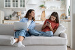 © DimaBerlin - Independent teenage girl trying to hide phone screen from mother sits on sofa. Curious attentive woman looking after daughter who uses internet messengers and making acquaintances in social networks
