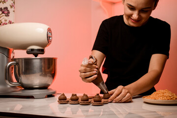 Wall Mural - Smiling confectioner squeezes brown cream onto beige macaroon halves