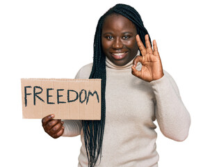 Poster - Young black woman with braids holding freedom banner doing ok sign with fingers, smiling friendly gesturing excellent symbol