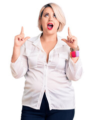 Wall Mural - Young blonde plus size woman wearing casual shirt amazed and surprised looking up and pointing with fingers and raised arms.