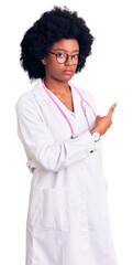 Poster - Young african american woman wearing doctor coat and stethoscope pointing with hand finger to the side showing advertisement, serious and calm face