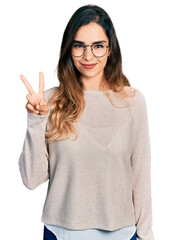 Wall Mural - Beautiful hispanic woman wearing casual sweater and glasses showing and pointing up with fingers number two while smiling confident and happy.