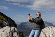 © Guzel - Gray-haired long-haired man with backpack taking selfie on steep slope on picturesque mountain background, Austria